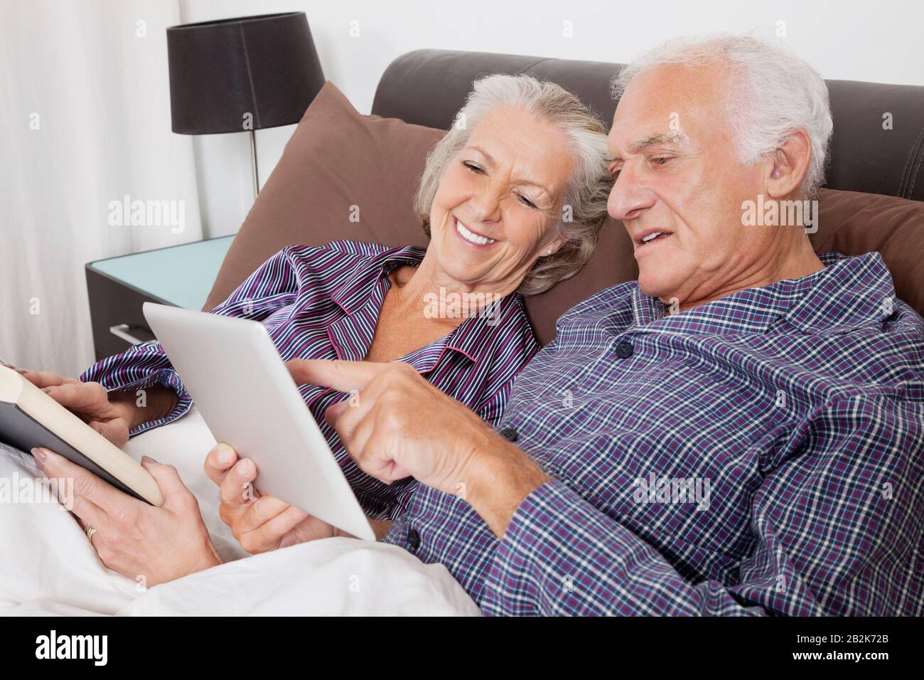 Happy senior couple using digital tablet while lying on bed in room Stock Photo