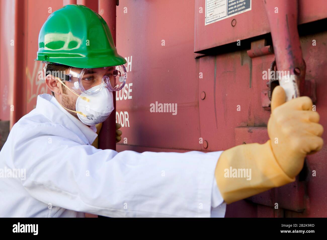 Worker in hazmat suit, hard-hat and face mask closing metal door Stock Photo
