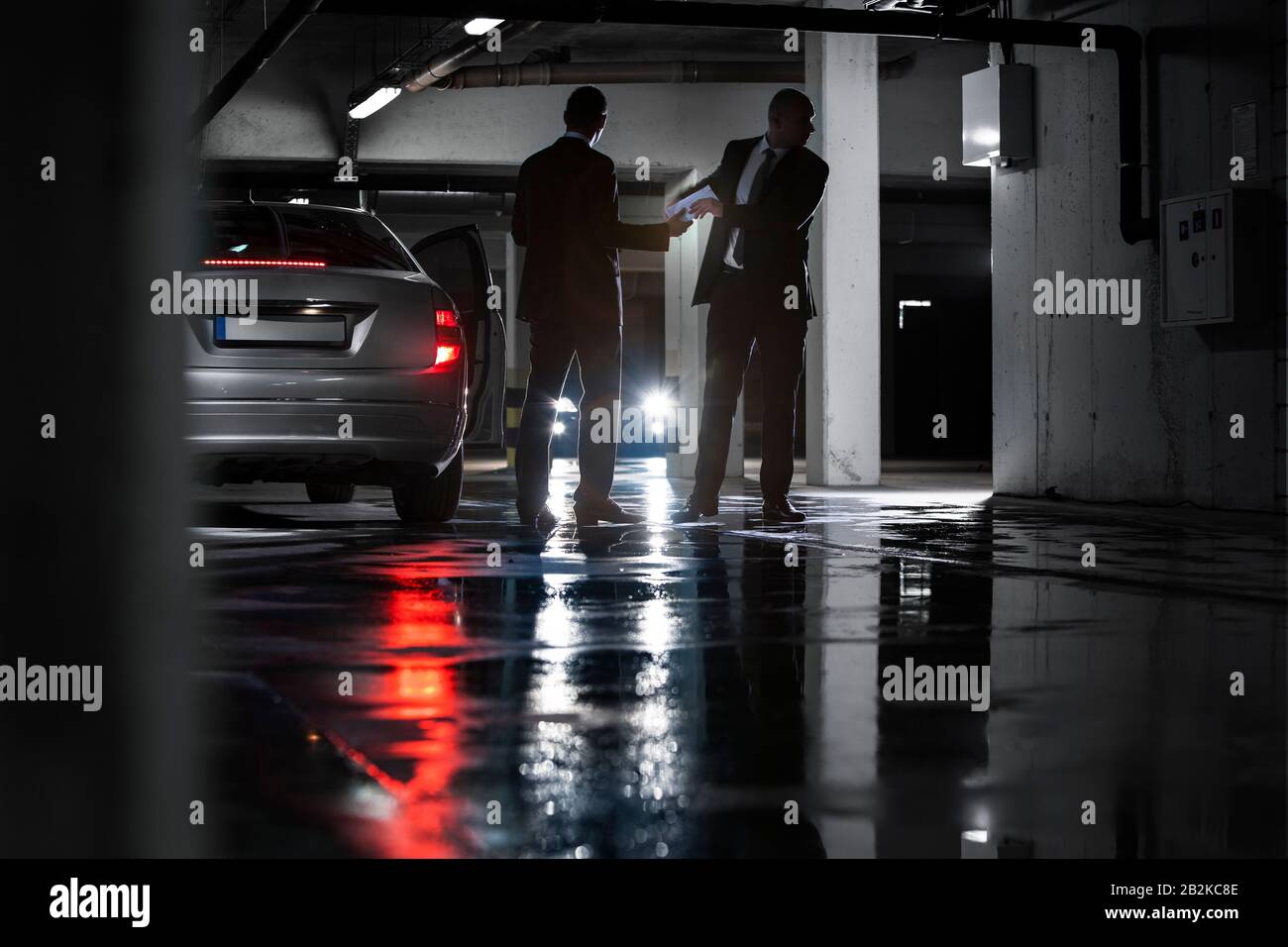 Full length of businessmen giving and receiving envelop in basement ...