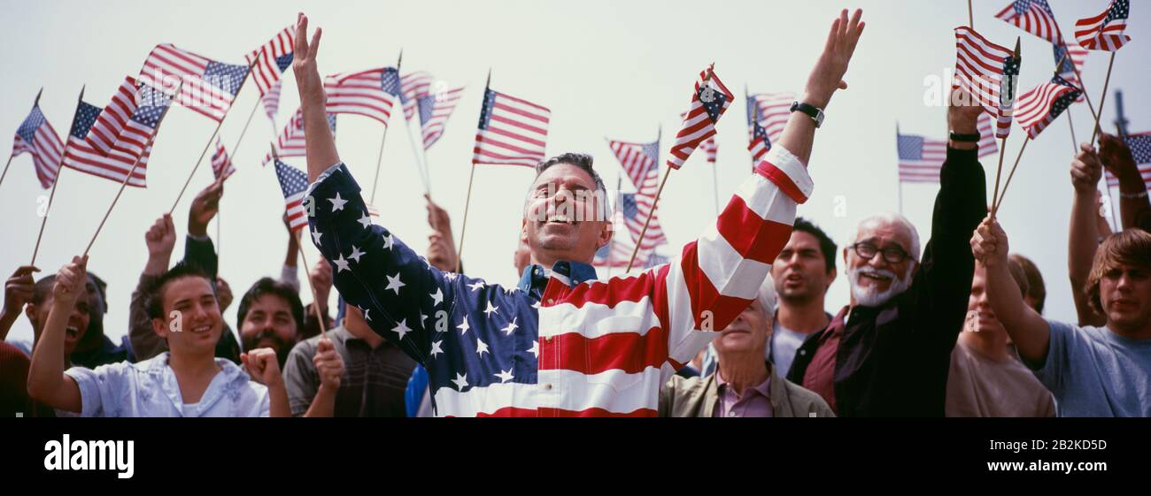 Happy mid adult man with crowd waving North American flags in background Stock Photo