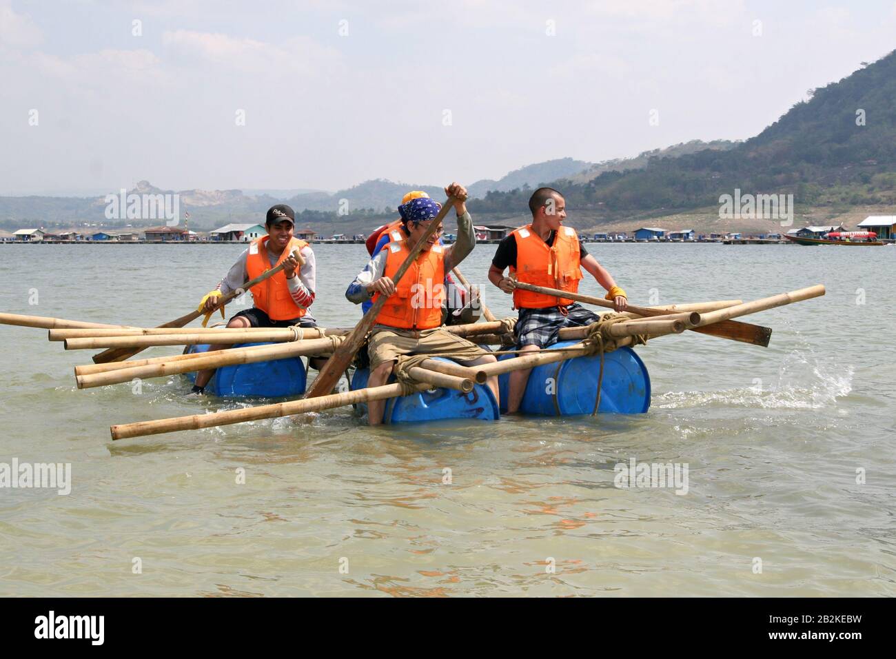 A group of young people are rowing an emergency boat made of bamboo sticks, plastic barrels and ropes in an outdoor survival training. Stock Photo