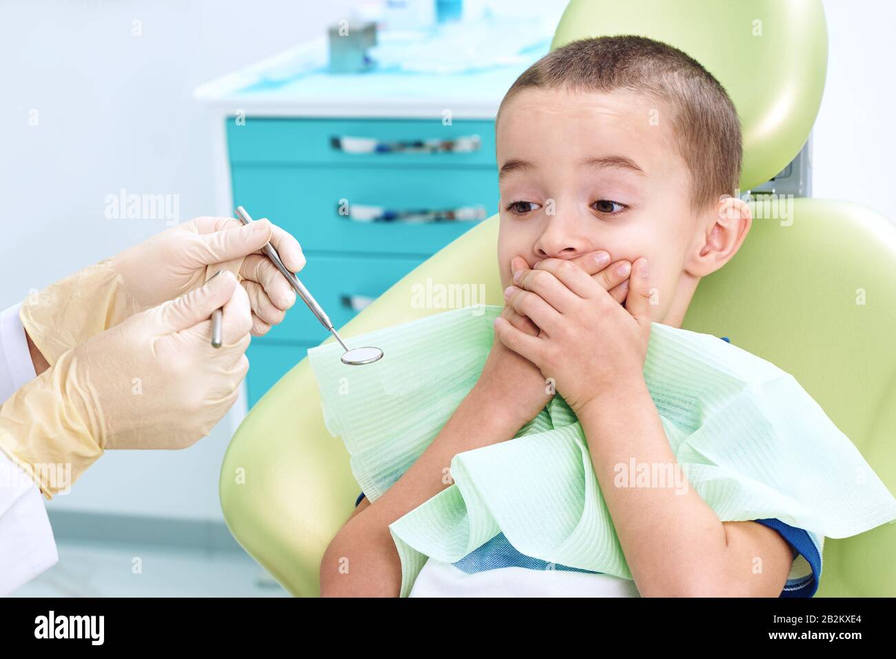 Portrait of a scared child in a dental chair. The boy covers his mouth with his hands, afraid of being examined by a dentist. Children's dentistry. Stock Photo