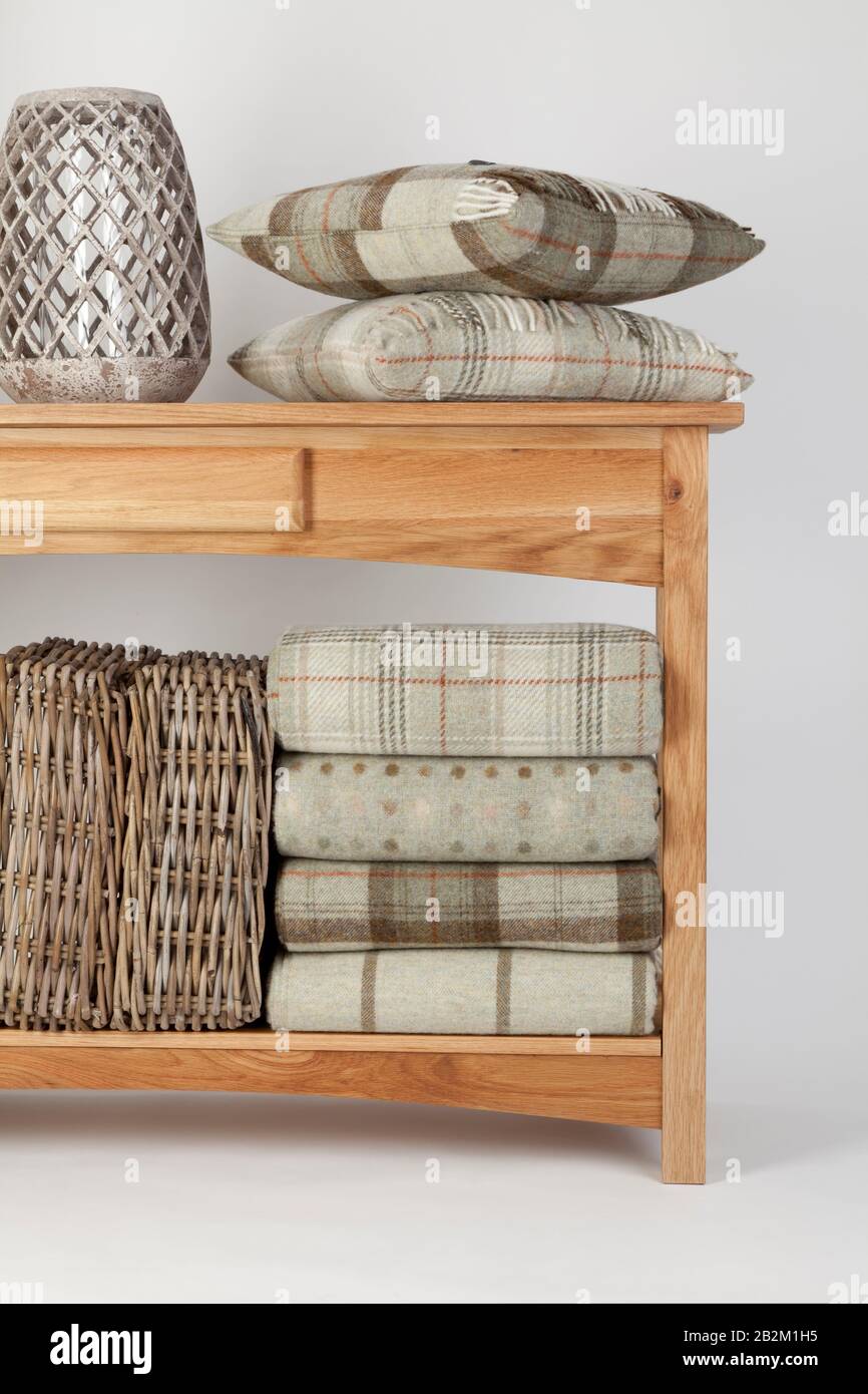 Sideboard style wooden beach table with natural coloured cushions, throws and ornaments and wicker baskets on a white background Stock Photo