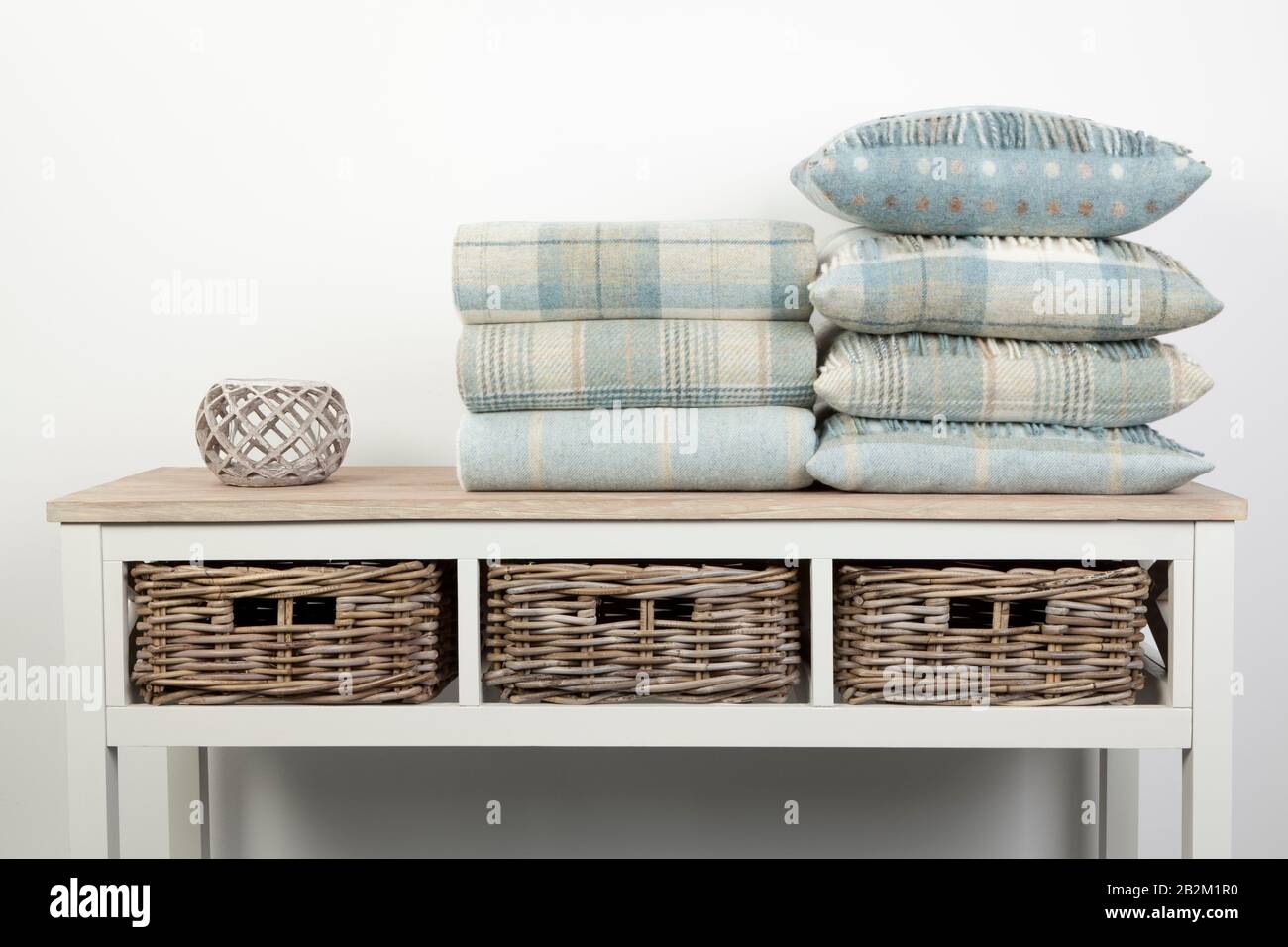 Sideboard style white wooden table with blue coloured cushions, throws and ornaments and wicker baskets on a white background Stock Photo