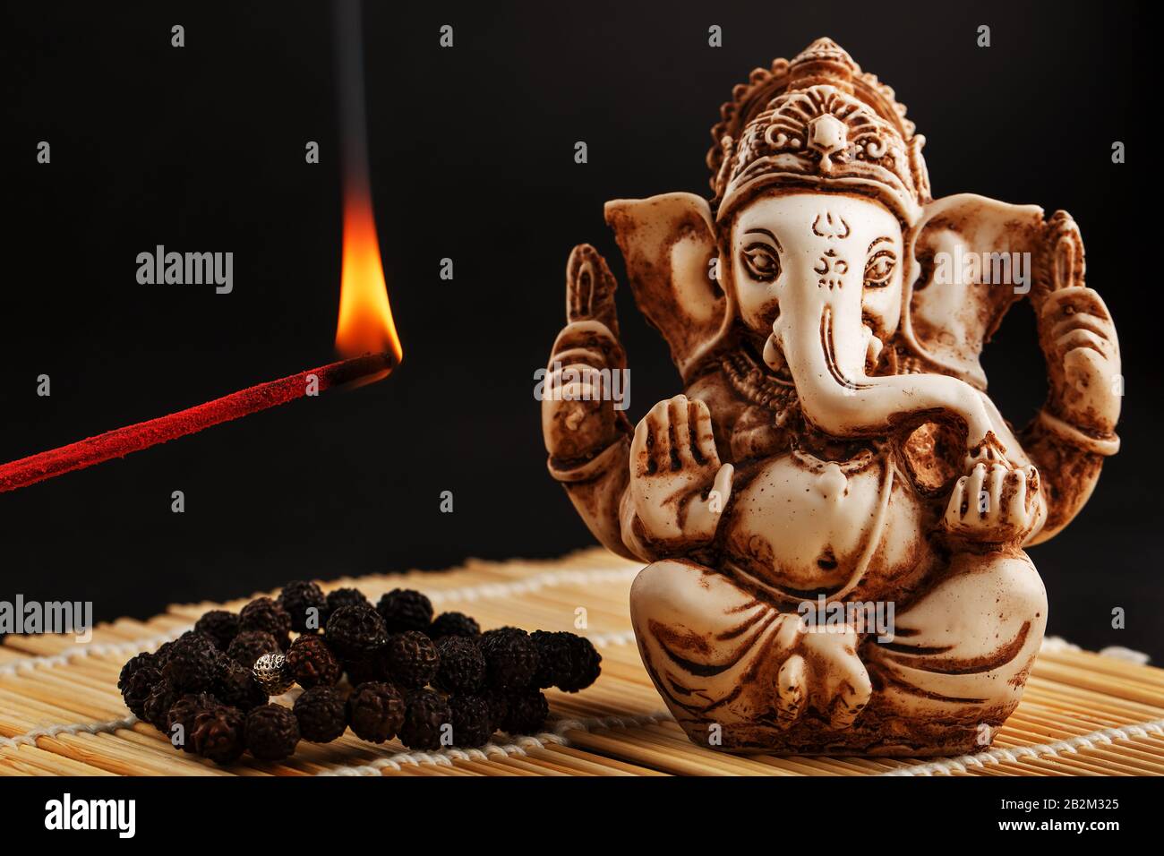 Hindu god Ganesh on a black background. Rudraksha statue and rosary on a  wooden table with a red incense stick and incense smoke. Copy space Stock  Photo - Alamy