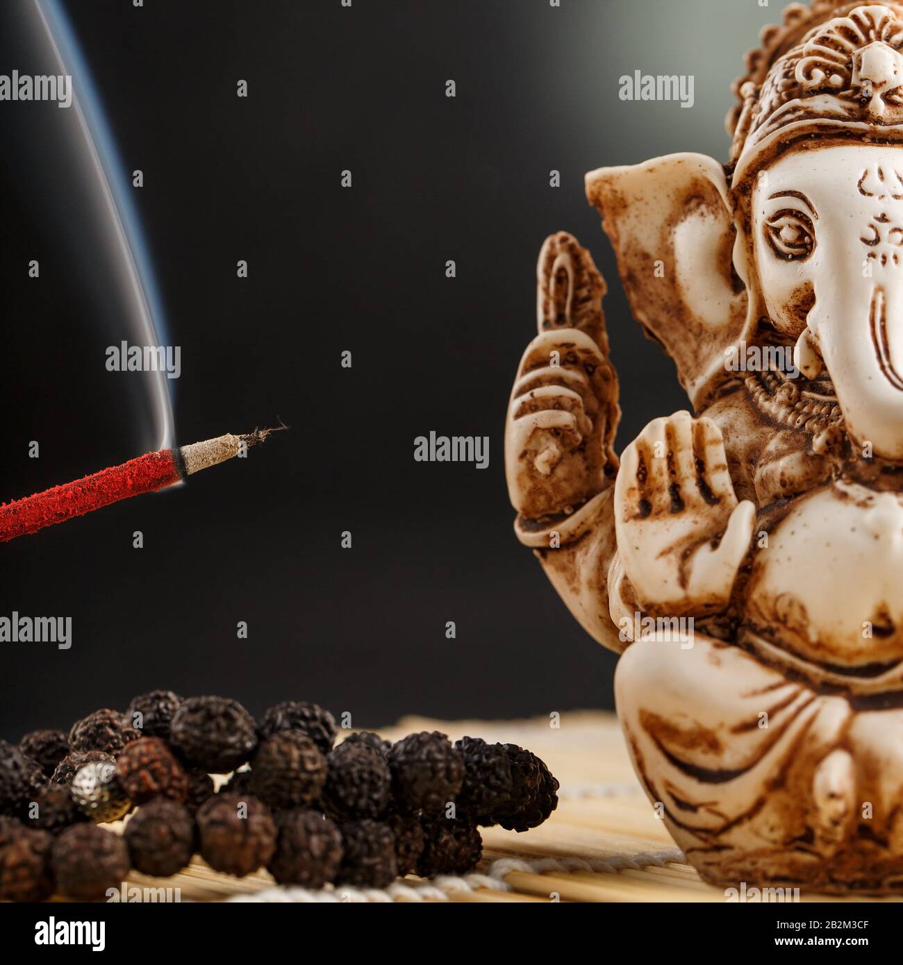 Hindu god Ganesh on a black background. Rudraksha statue and rosary on a  wooden table with a red incense stick and incense smoke. Copy space Stock  Photo - Alamy