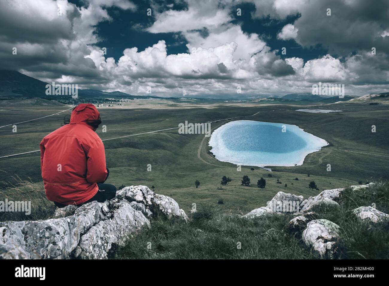 Female in sportswear sitting on the top of mountain and enjoy in the beautiful view on the landscape with lake.  Devil Eye Lake at Durmitor Mountain Stock Photo