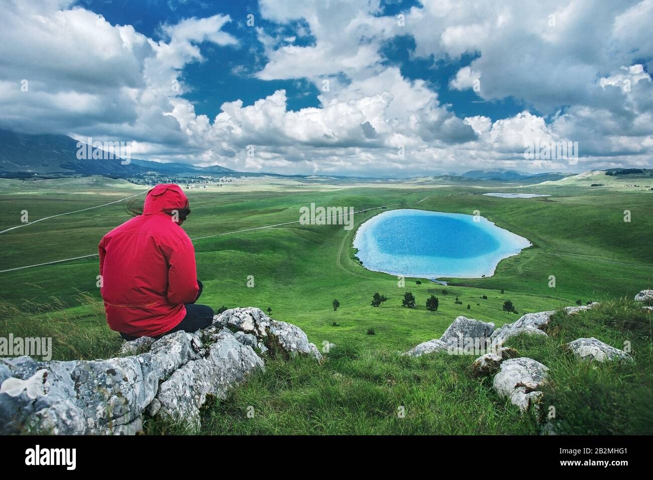 Female in sportswear sitting on the top of mountain and enjoy in the beautiful view on the landscape with lake.  Devil Eye Lake at Durmitor Mountain Stock Photo