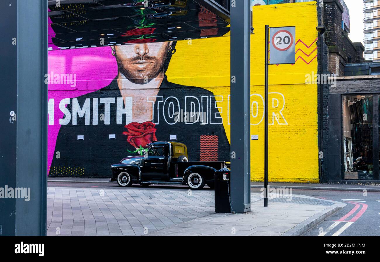 A 1950's Chevy 3100 pickup truck drives past a huge piece of graffiti art in Shoreditch in East London. Stock Photo