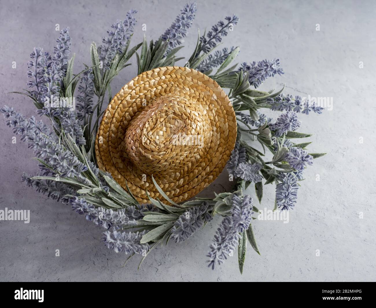 Lay flat photography of a straw cowgirl or cowboy hat sitting on top of a purple lavender flower plant wreath against a white gray plaster background. Stock Photo