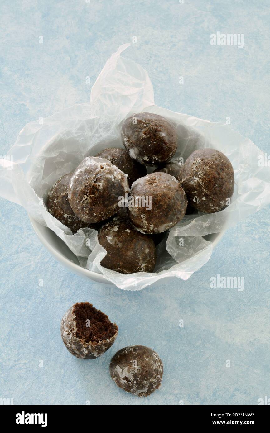Fresh glazed chocolate donut holes in white bowl with crumpled wax paper on light blue background in vertical format Stock Photo