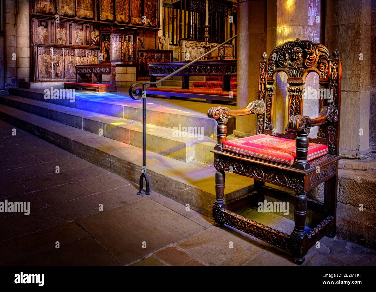 Antique wooden chair in the sunlit interior of Hexham Abbey. Sunshine throuf stained glass causing dappled patterns of coloured light on stone steps. Stock Photo