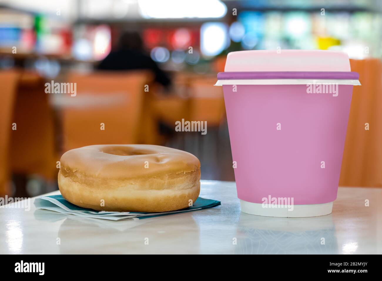 A pink disposable cup with coffee and a donut on a coffee shop table Stock Photo