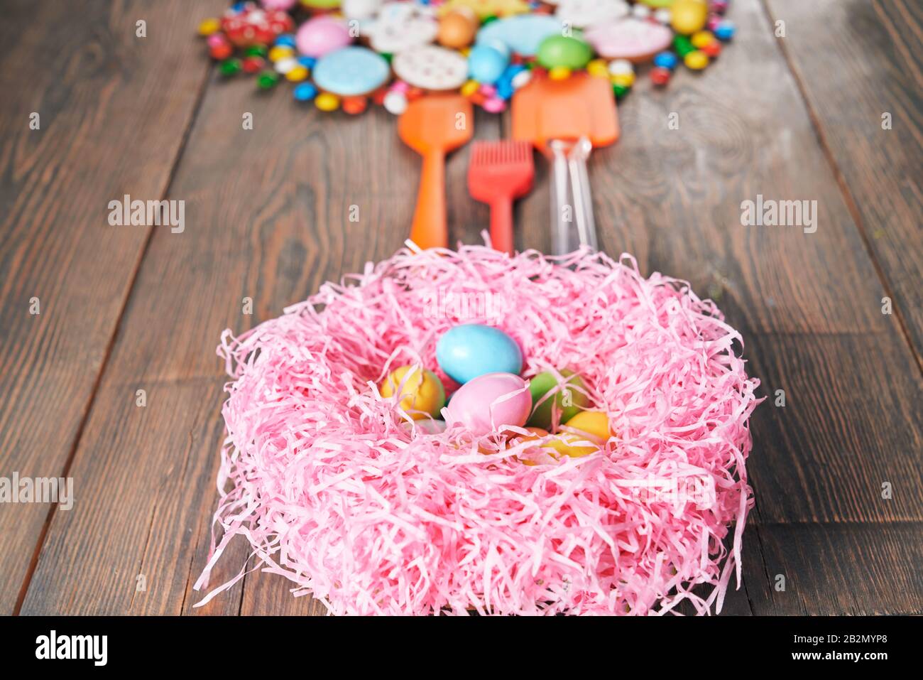 Colorful ginger glazed cookies, chocolate balls with sugar shell and silicone spatulas. Selective focus of nest with eggs and homemade pastry of easte Stock Photo