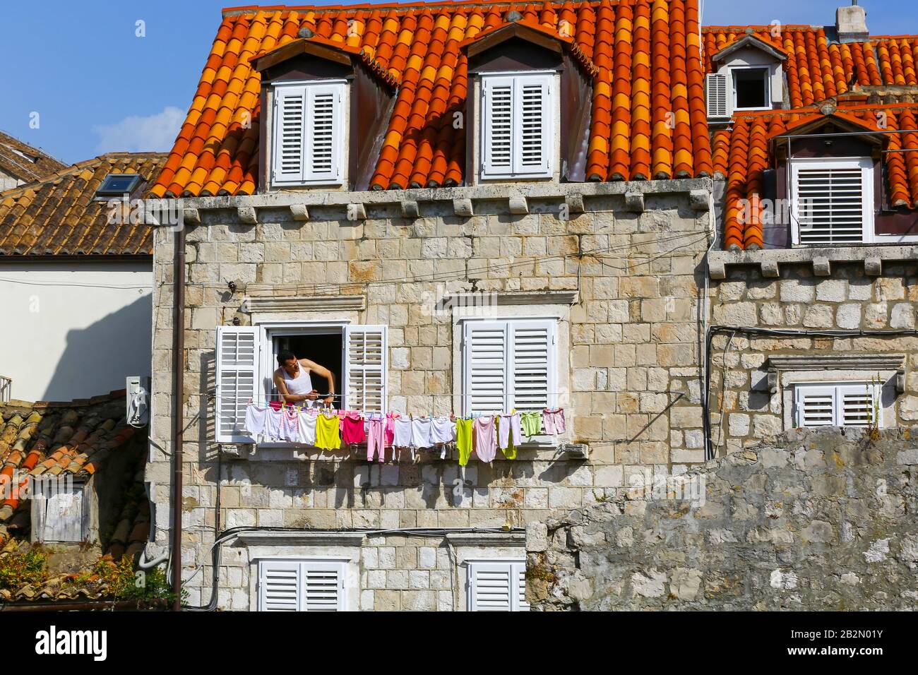 A man looking out of his window with colourful washing hanging from the window in the Old Town, Dubrovnik, Croatia Stock Photo