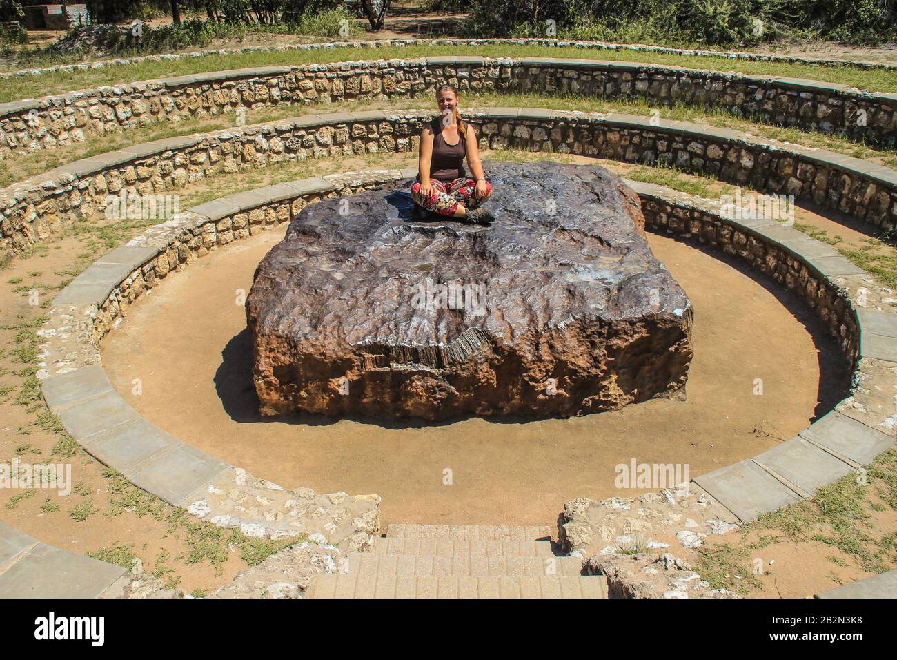 The largest meteorite in the world at Grootfontein, Namibia. A huge piece of iron from space. White girl tourist sitting on a meteorite Stock Photo