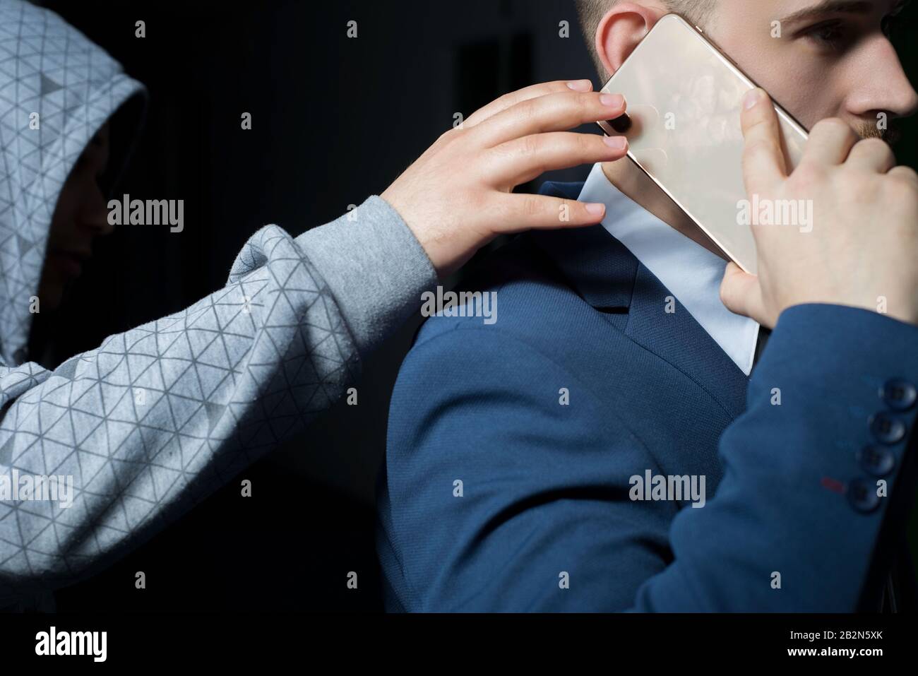 close-up, portrait of a handsome bearded guy, an ibisman in a business suit talking on a smartphone, from behind a thief in a hood reaches out with hi Stock Photo