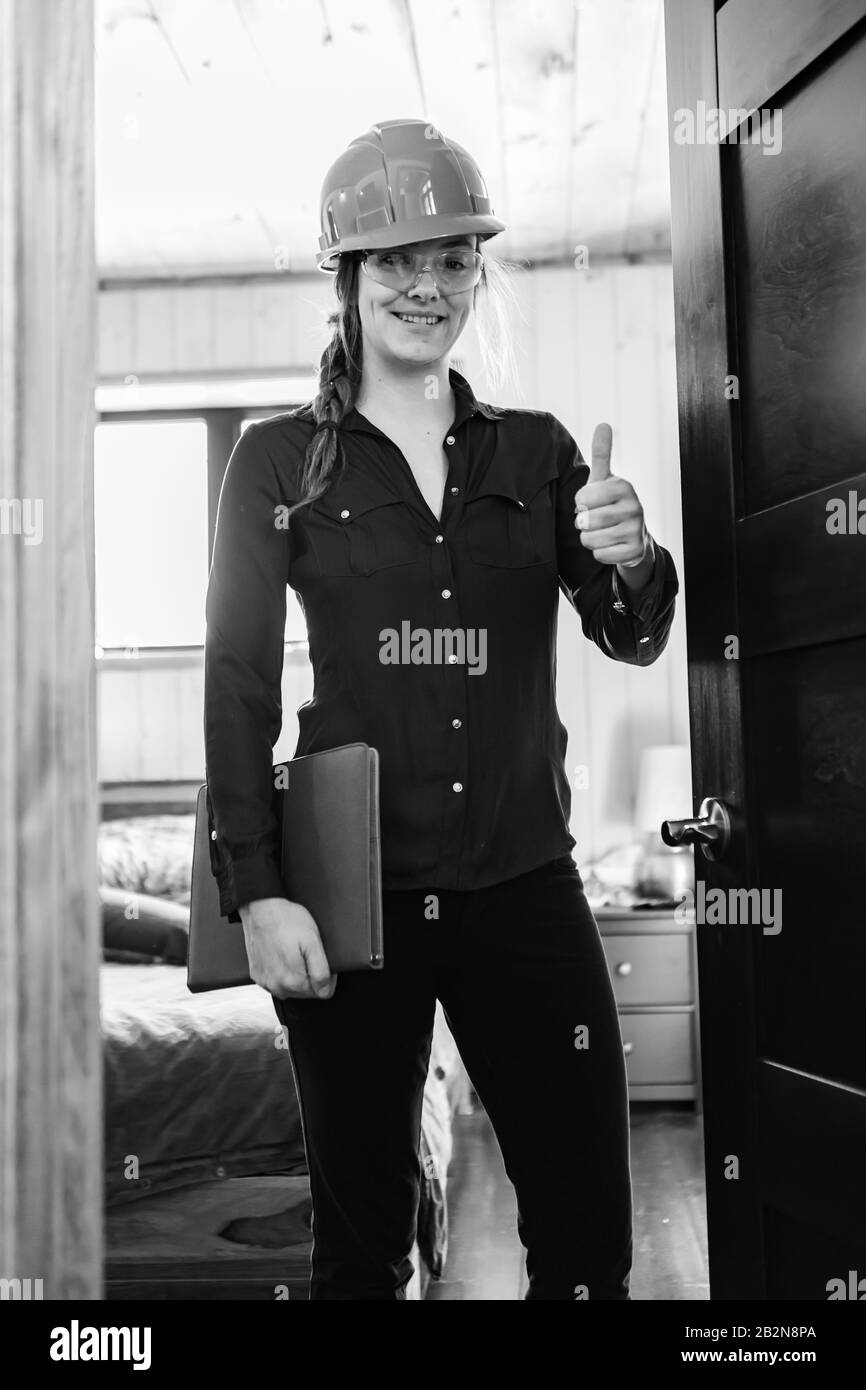 happy female inspector smiling and giving thumb up as she holding a clipboard during a modern home air quality inspection. vertical black and white. Stock Photo