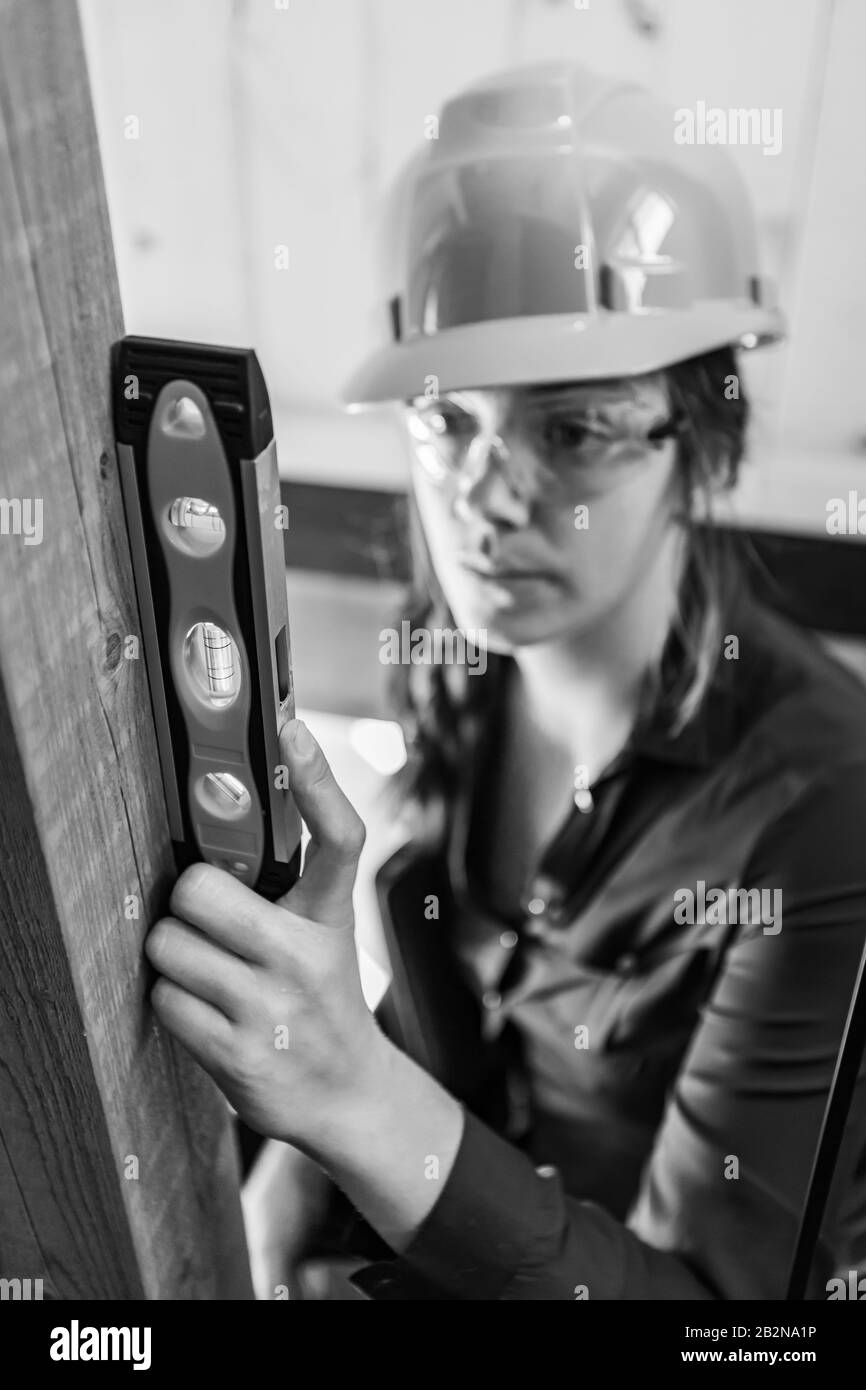 selective focus of spirit level on woman's hand, she is a female inspector wearing hard hat during a pre-purchase inspection. vertical black and white Stock Photo