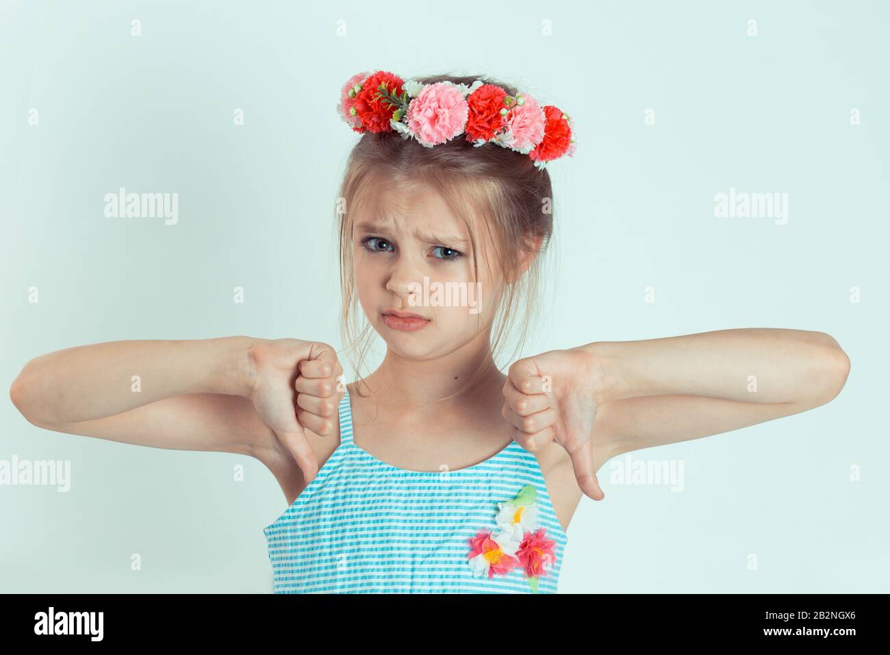 Girl kid showing thumbs down gesture. Body language, human emotion face expression. Closeup portrait of Caucasian kid model with floral headband isola Stock Photo