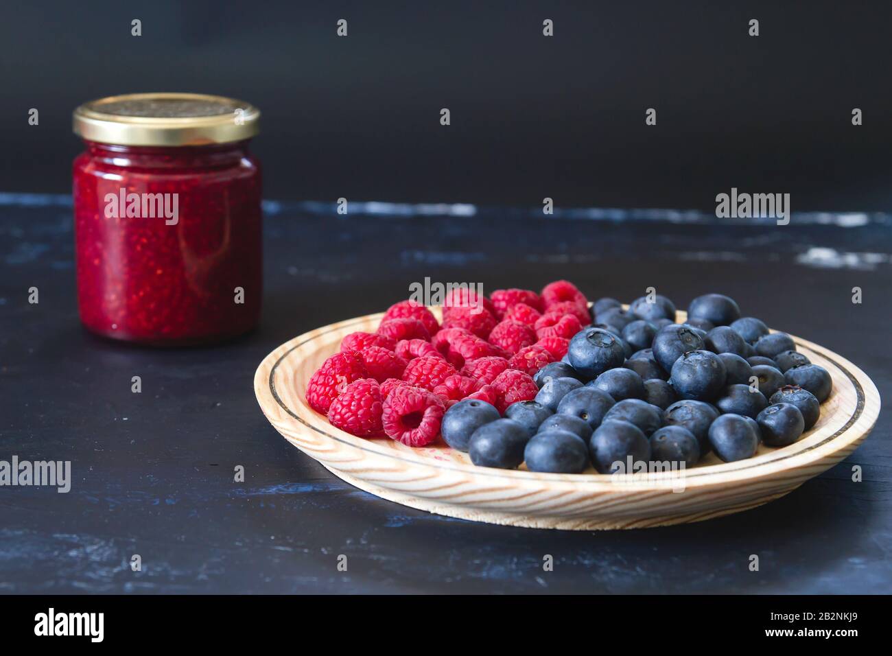 Homemade jam and fresh blueberries and raspberries on wooden dish Stock Photo