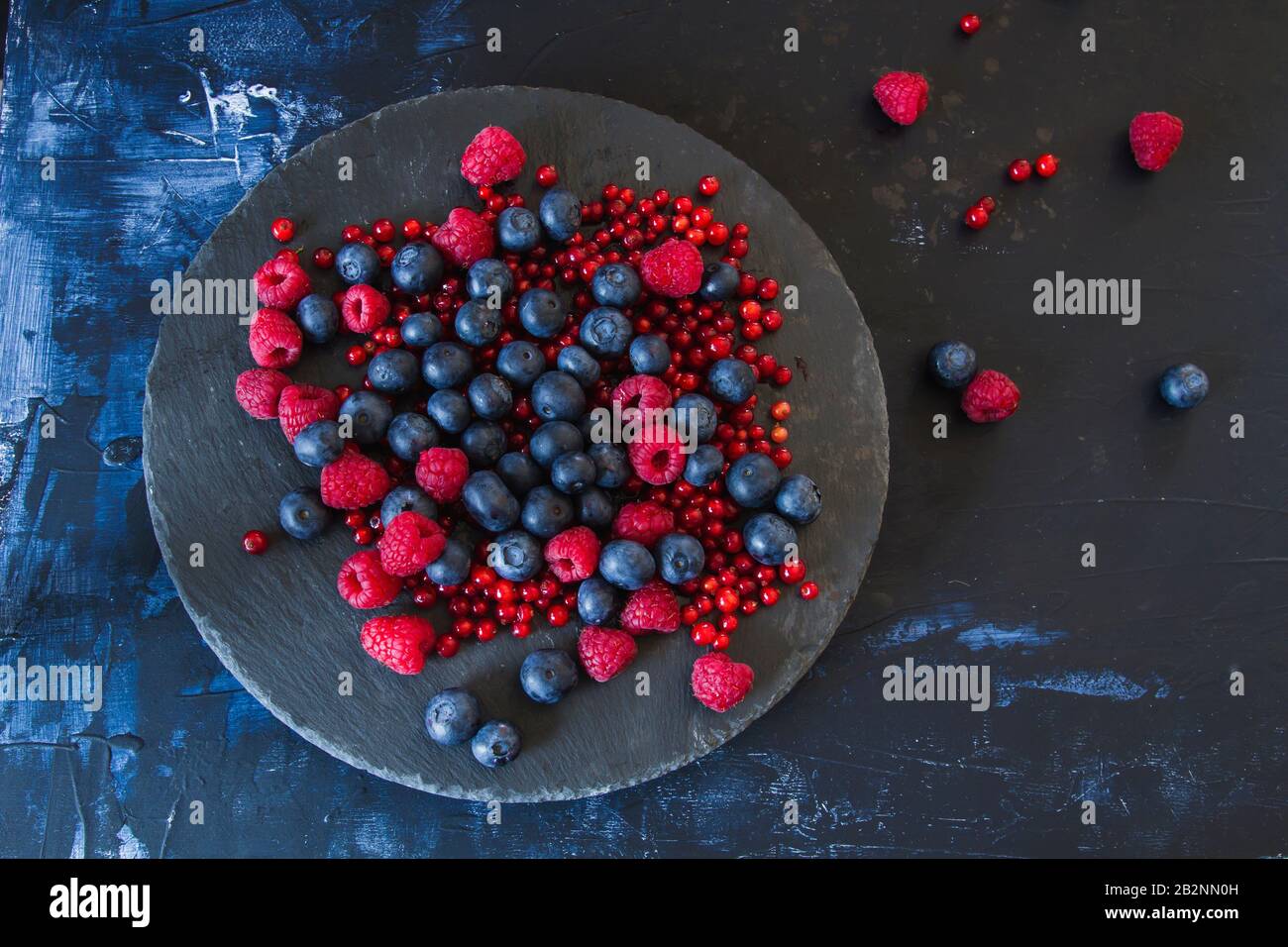 Fresh blueberries, raspberries and redcurrants, black dish, dark backdrop Stock Photo