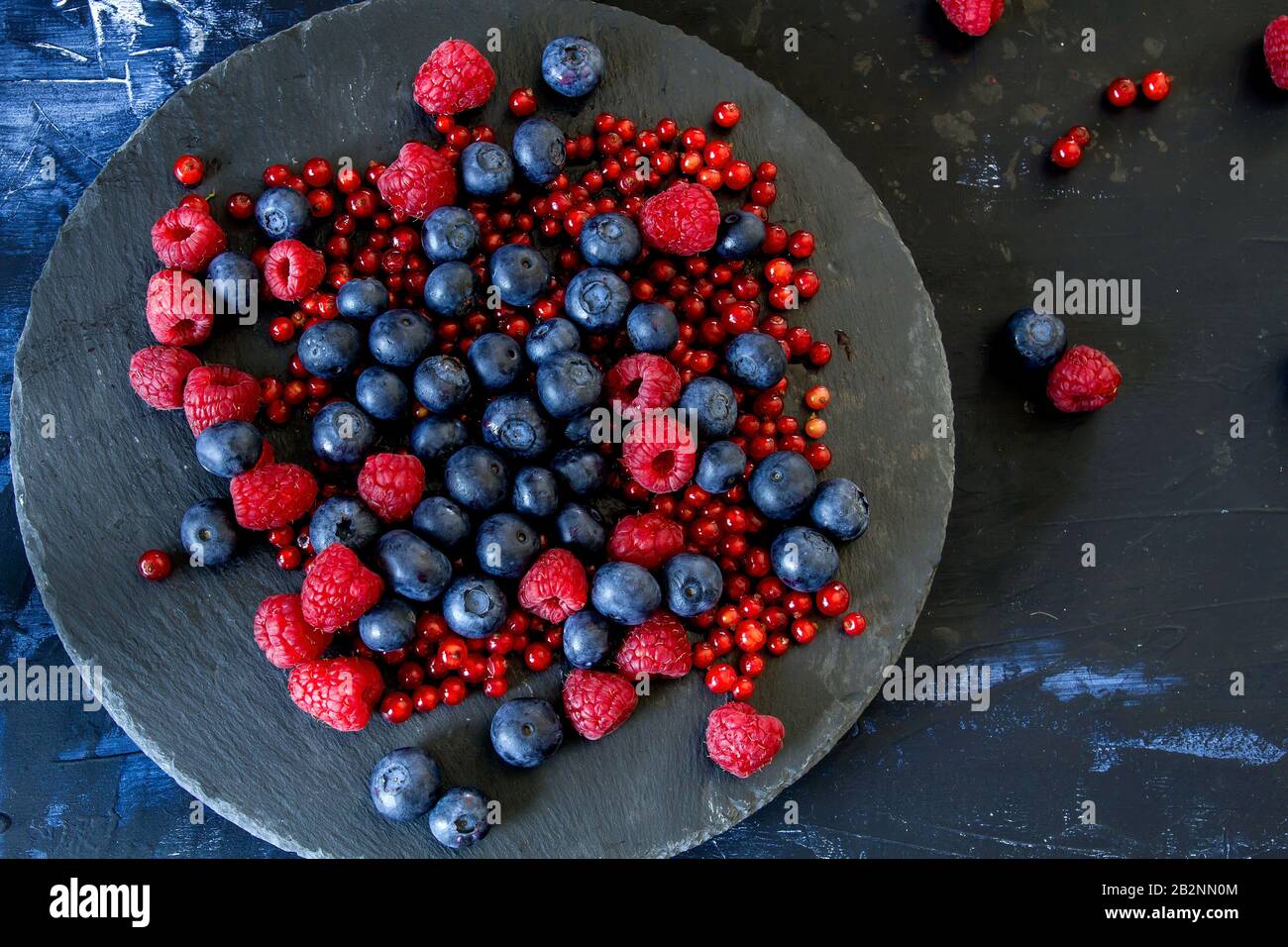 Fresh blueberries, raspberries and redcurrants, black dish, dark backdrop Stock Photo