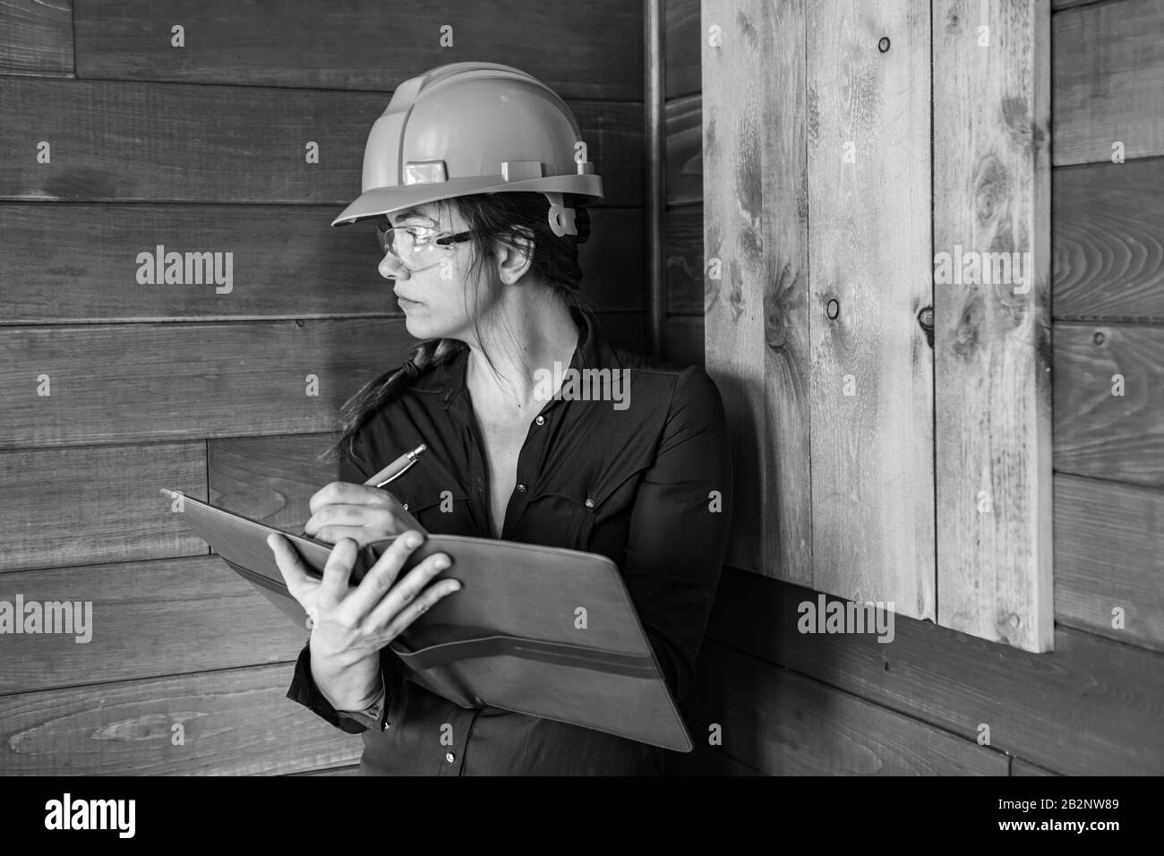 inspector woman taking notes on clipboard during Indoor air quality inspection she looking for molds, fungi problems on wooden walls, black and white Stock Photo