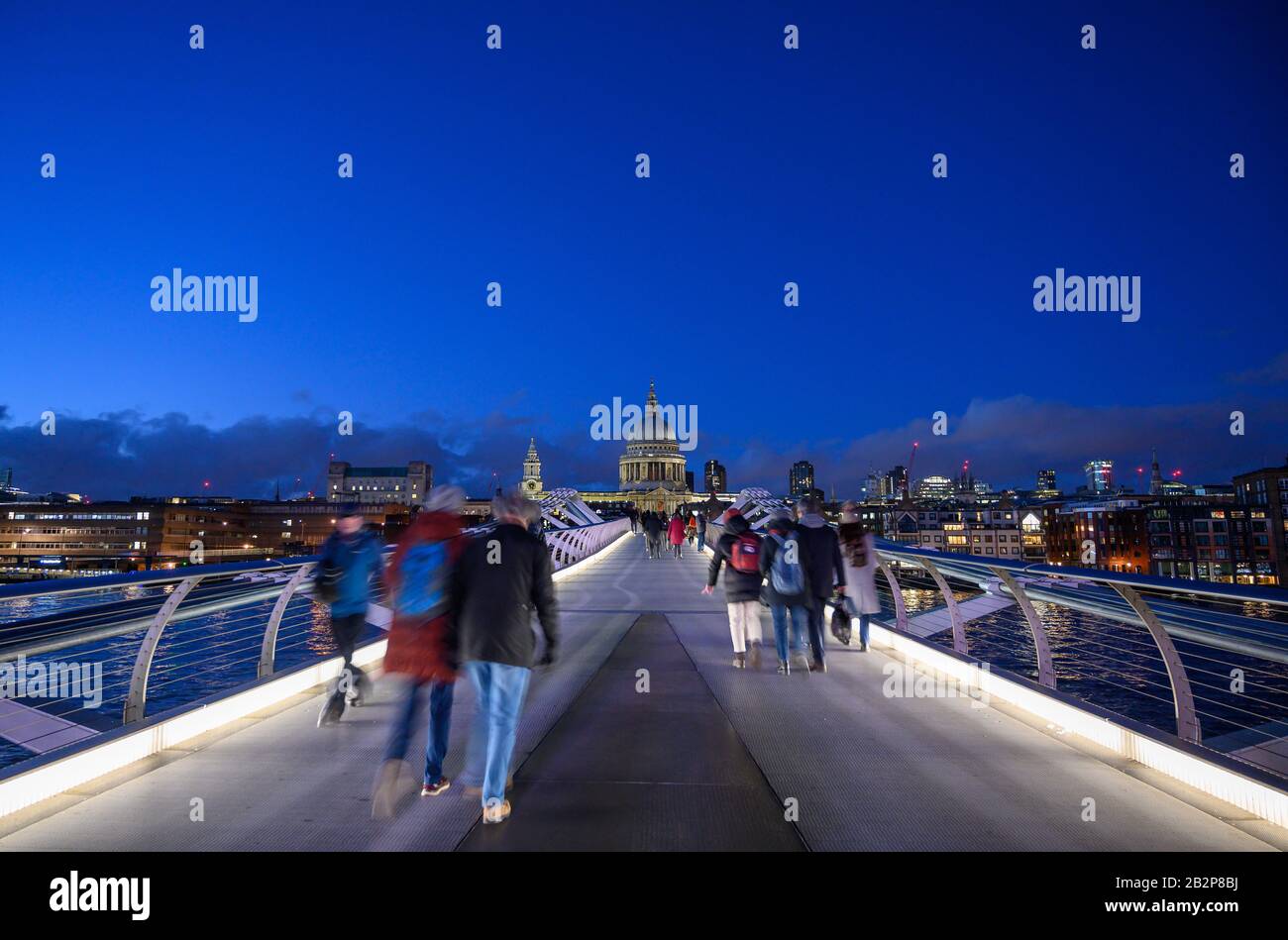 Night view of the Millennium Bridge and St Paul's Cathedral in London, UK. Unrecognisable people walk across the bridge (motion blur). Stock Photo
