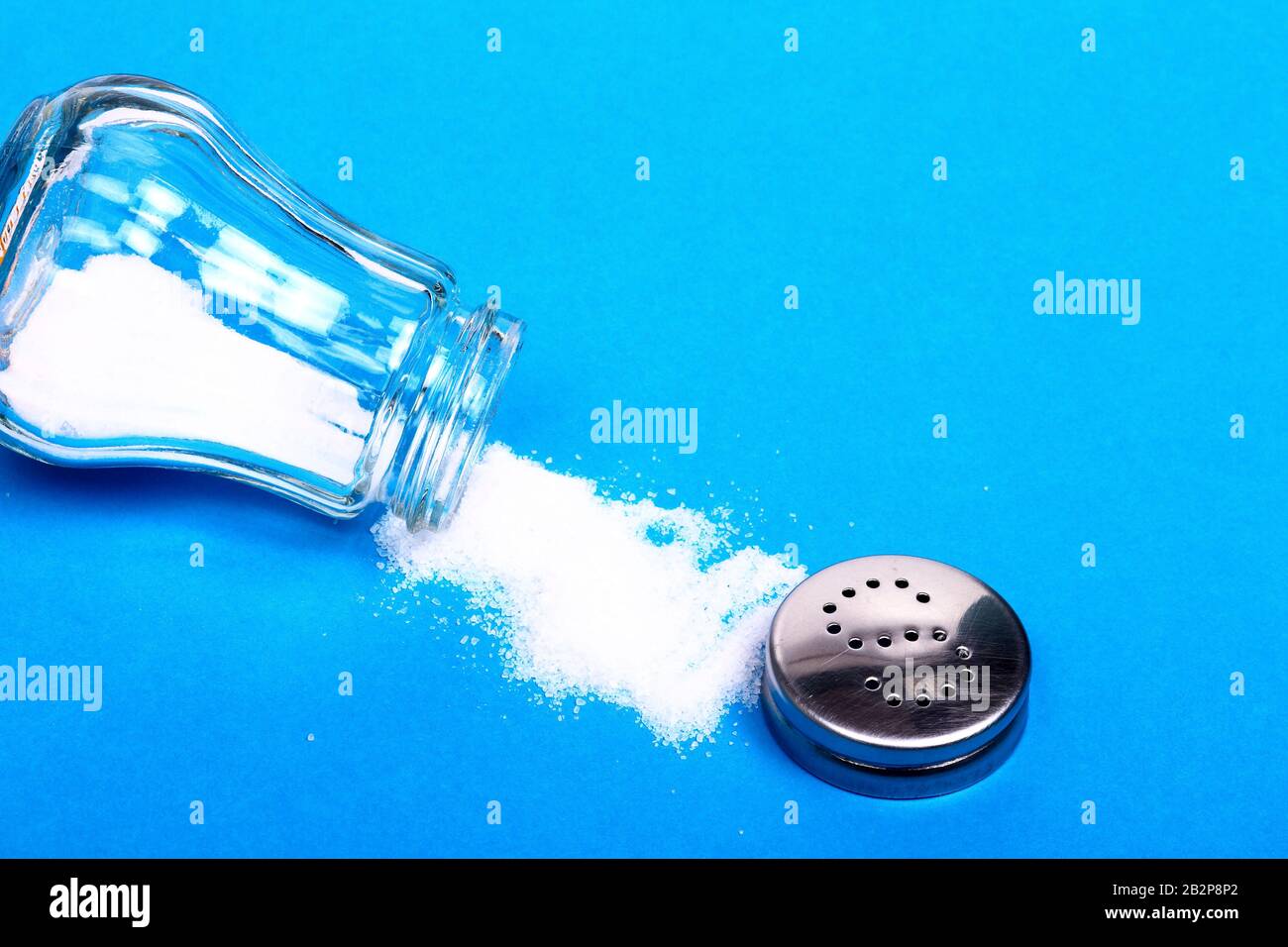 https://c8.alamy.com/comp/2B2P8P2/salt-spilling-out-from-a-glass-sat-shaker-isolated-on-a-blue-background-with-copy-space-2B2P8P2.jpg