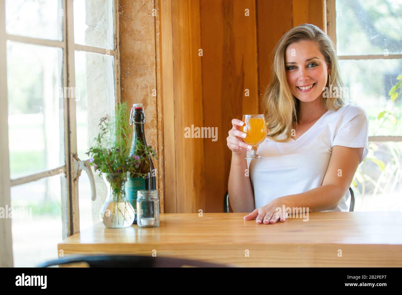 Casual lifestyle portrait of a beautiful woman lounging relaxed at local pub brewery with friends, drinking craft beer Stock Photo