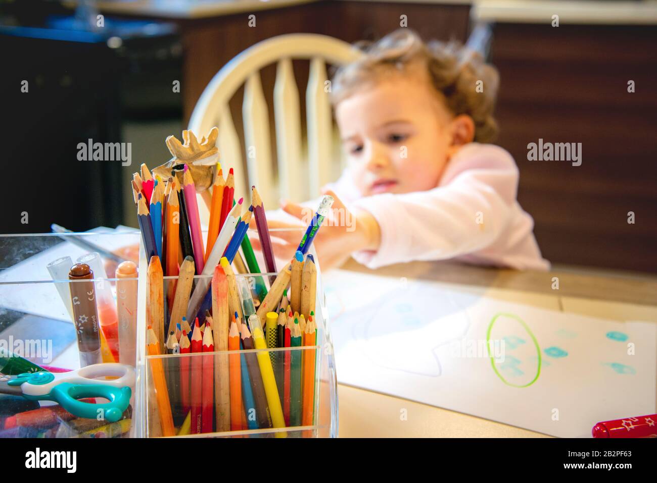 colored pencils in the foreground in focus, child reaching across to select different one. Stock Photo