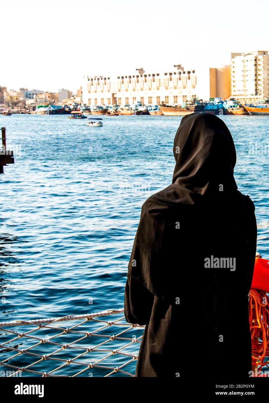 Back view of woman in black traditional abaya looking out across the Dubai Creek UAE Stock Photo