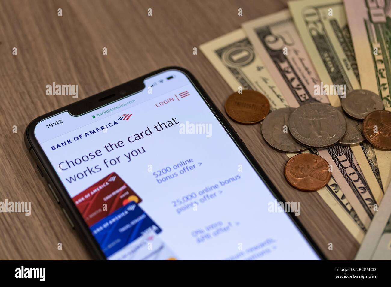 Bank of America logo atop of their website on a smartphone beside a pile of American cash and change on a desk. Stock Photo