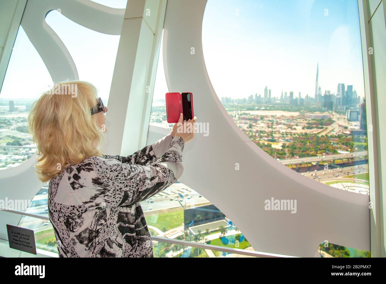 Middle age woman taking photograph of city landscape on her mobile phone from Dubai Frame UAE Stock Photo