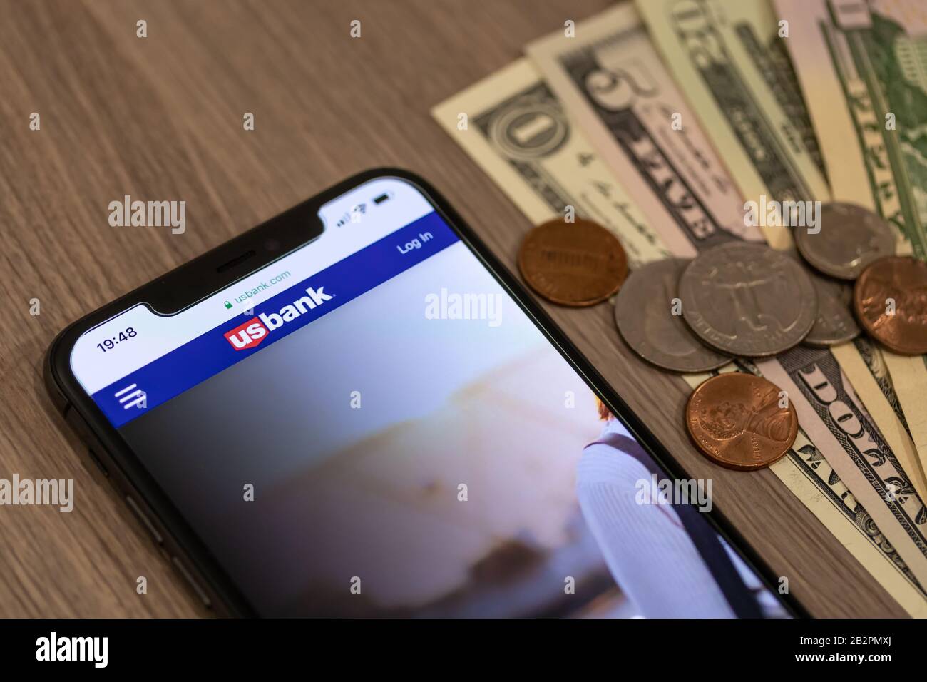 U.S. Bank logo atop of their website on a smartphone beside a pile of American cash and change on a desk. Stock Photo