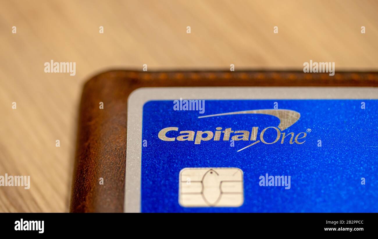 Capital One logo on a silver / blue credit card while placed atop of a wallet on a table. Stock Photo