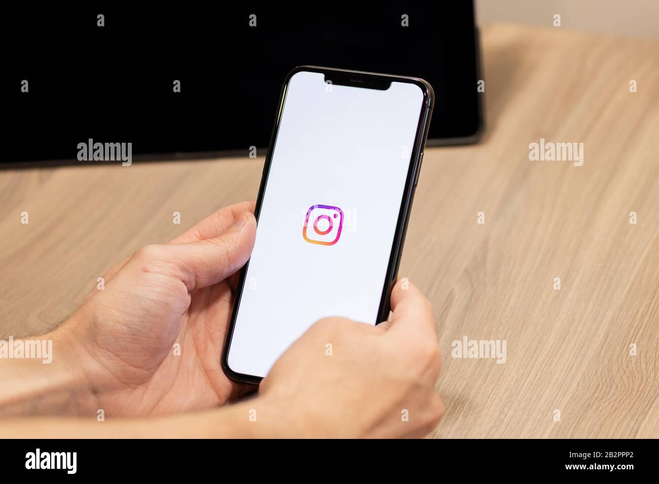 Man sitting at a table using an iPhone with a colourful Instagram logo on screen. Stock Photo