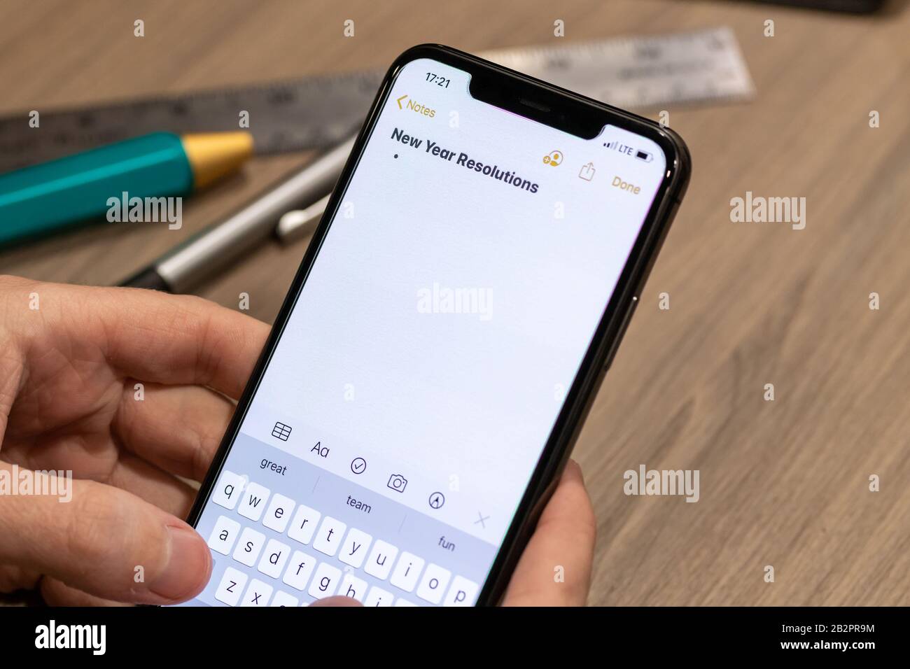 Man typing a note on a smartphone titled “New Year Resolutions” while sitting a desk. Stock Photo