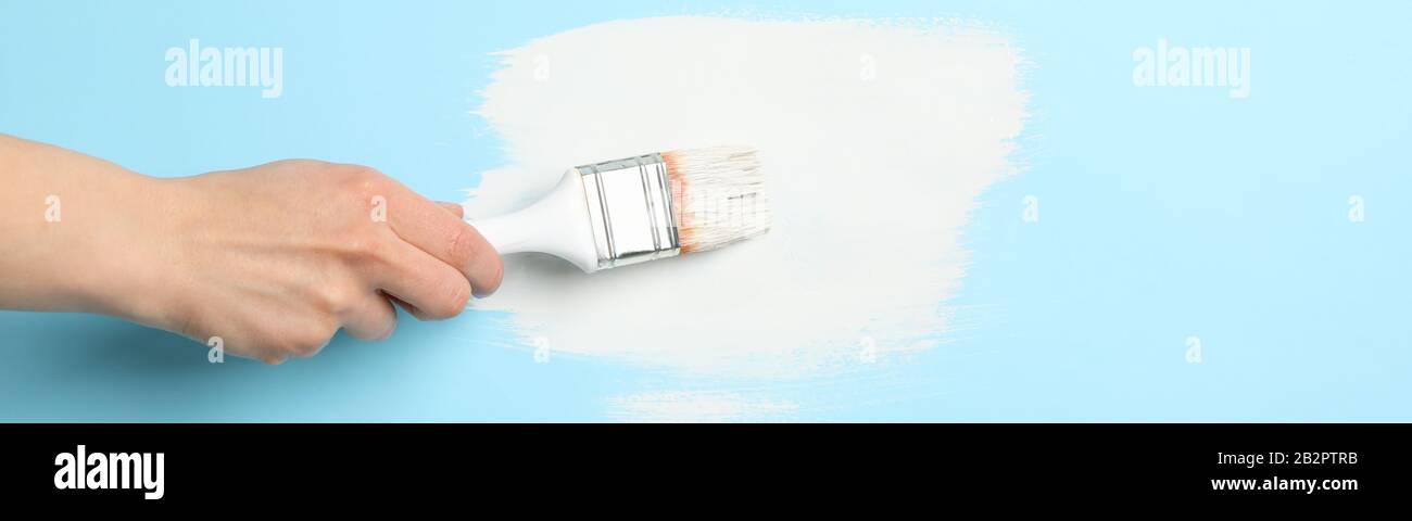 Female hand holding brush on blue background with white paint strokes ...