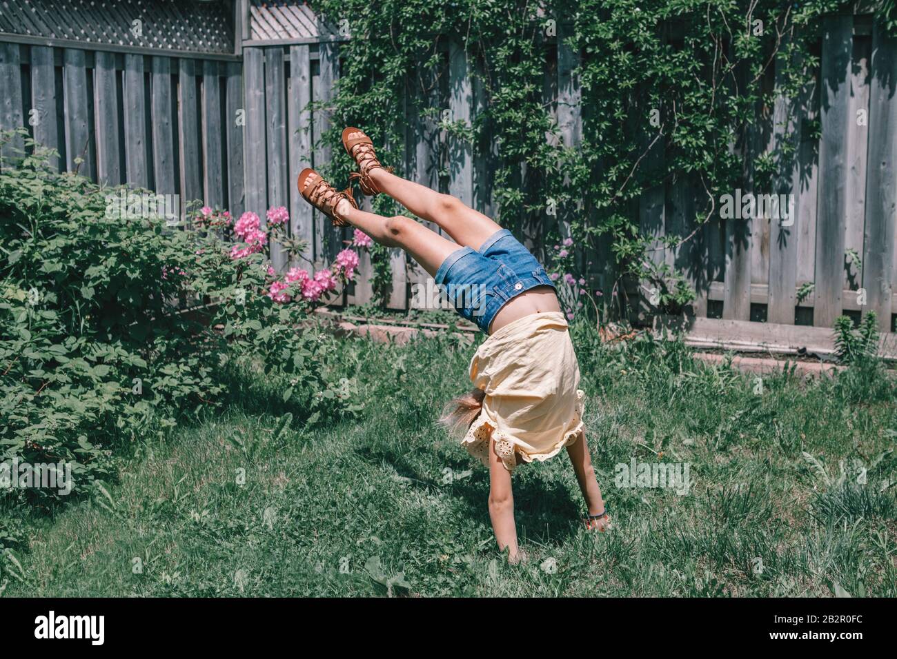 Funny child teenage girl doing cartwheel on backyard. Excited joyful kid playing outdoor. Happy lifestyle childhood and freedom spirit concept. Season Stock Photo