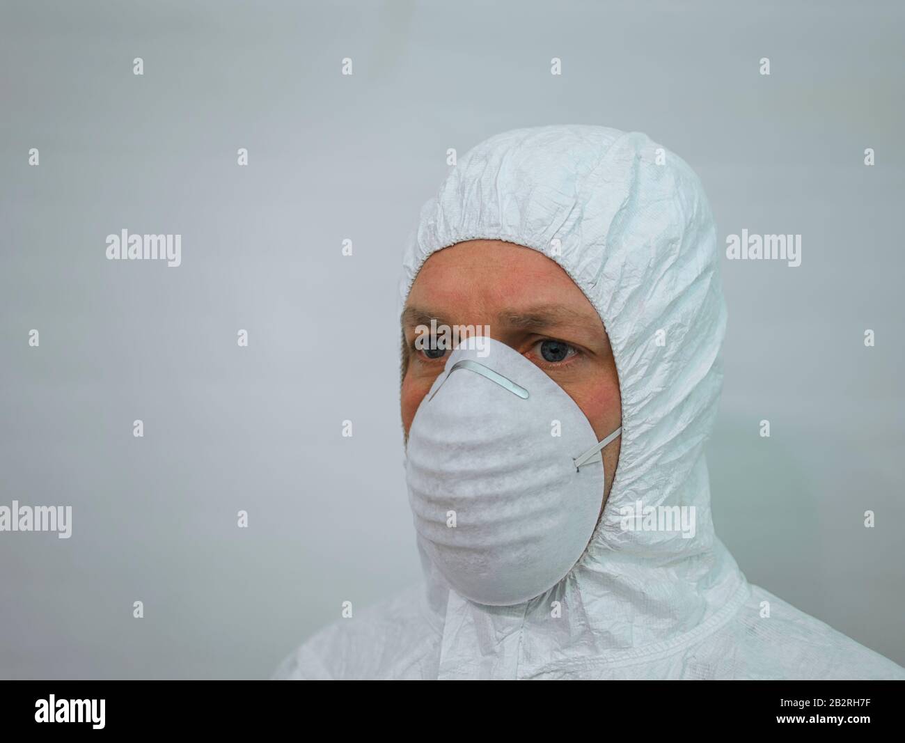 A man with a face mask and white hooded disposable overalls Stock Photo