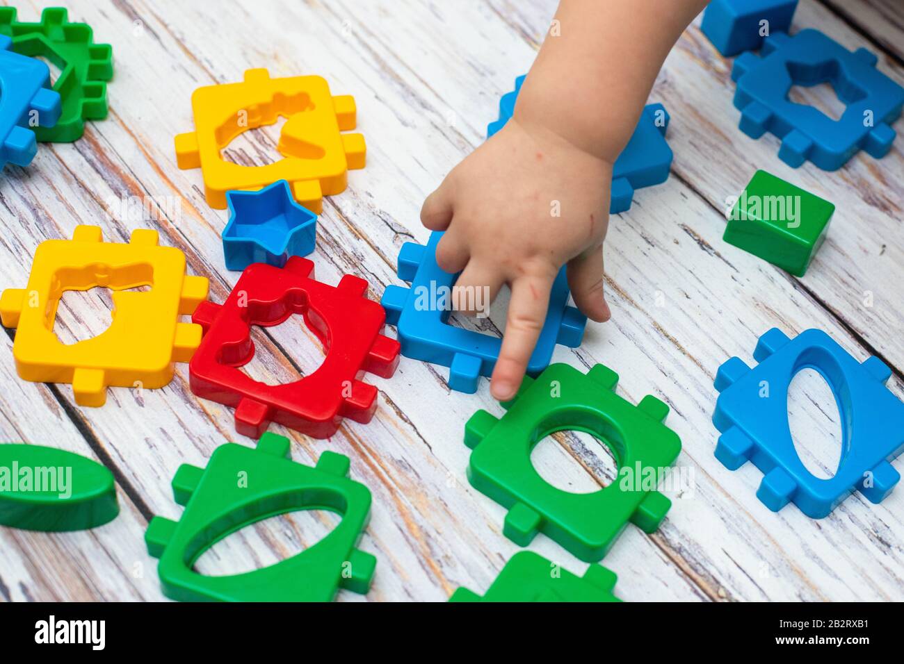 hand of child putting green action figure in Baby Blocks Shape Sorter Toy. Educational Sorting