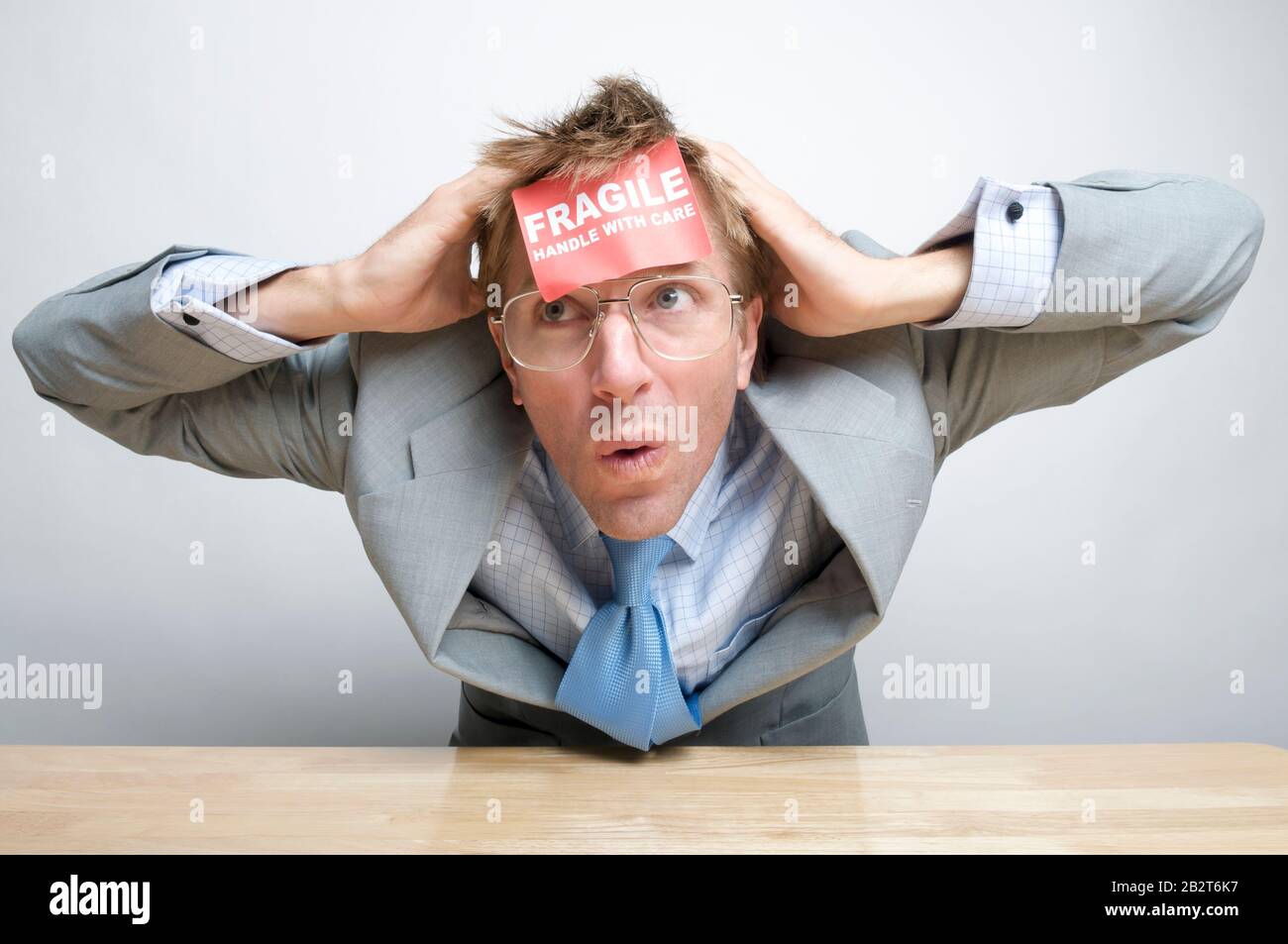 Worried office worker with a Fragile Handle With Care sticker sitting at his desk covering his head Stock Photo