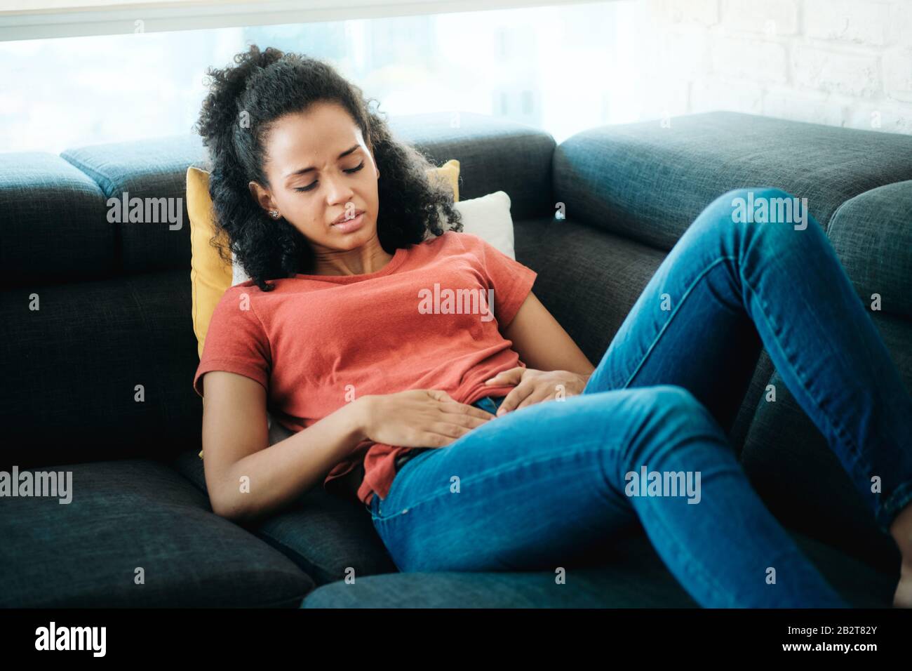 Young Black Woman With Menstrual Pain Lying On Sofa Stock Photo