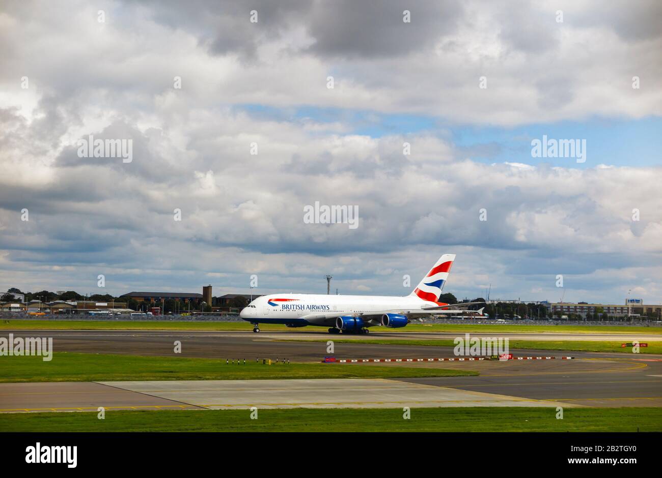 British Airways Airbus A380-861 in corporate livery taxiing on the runway in London Heathrow Airport viewed from Terminal 3 under dark gloomy clouds Stock Photo