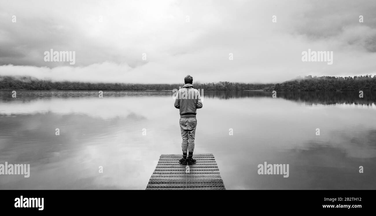 Young man standing on a jetty looking over a lake, foggy atmosphere, Lake Mapourika, West Coast, South Island, New Zealand Stock Photo