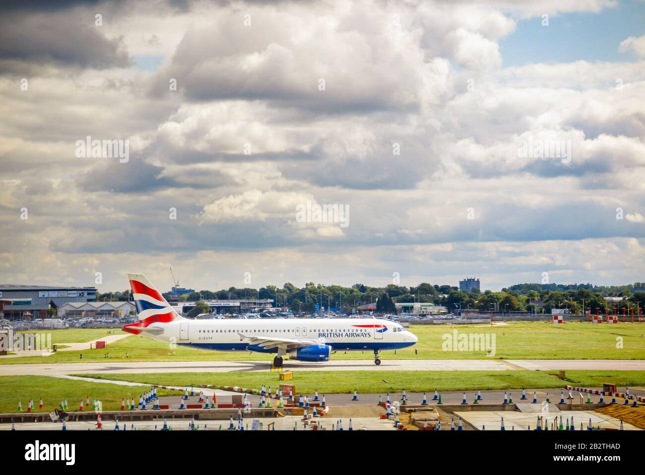 British Airways Airbus A320-232 in corporate livery standing on the runway in London Heathrow Airport viewed from Terminal 3 under dark gloomy clouds Stock Photo