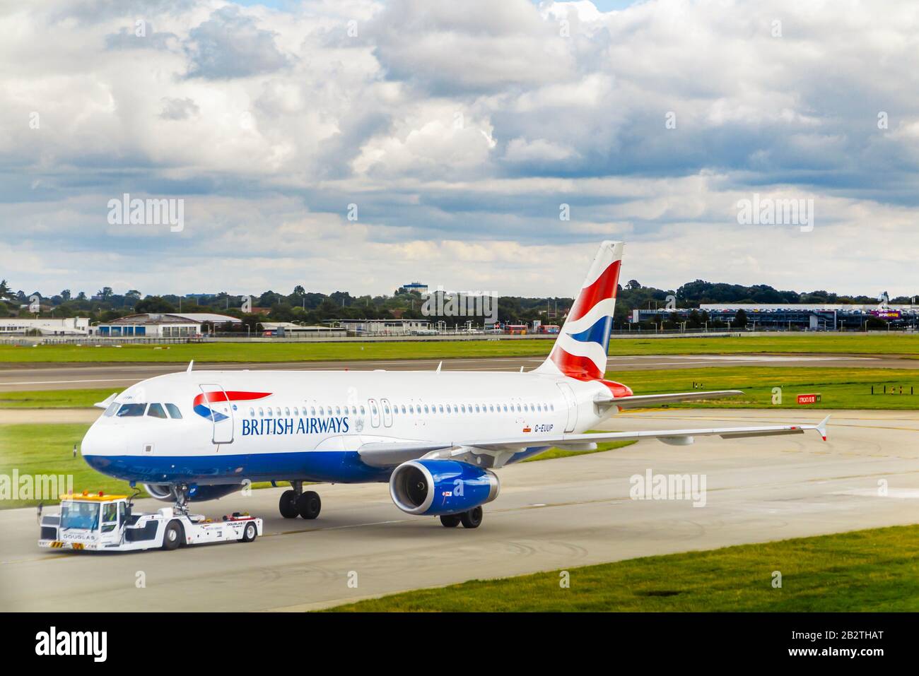 British Airways Airbus A320-232 in corporate livery being towed on the runway in London Heathrow Airport viewed from Terminal 3 under dark clouds Stock Photo