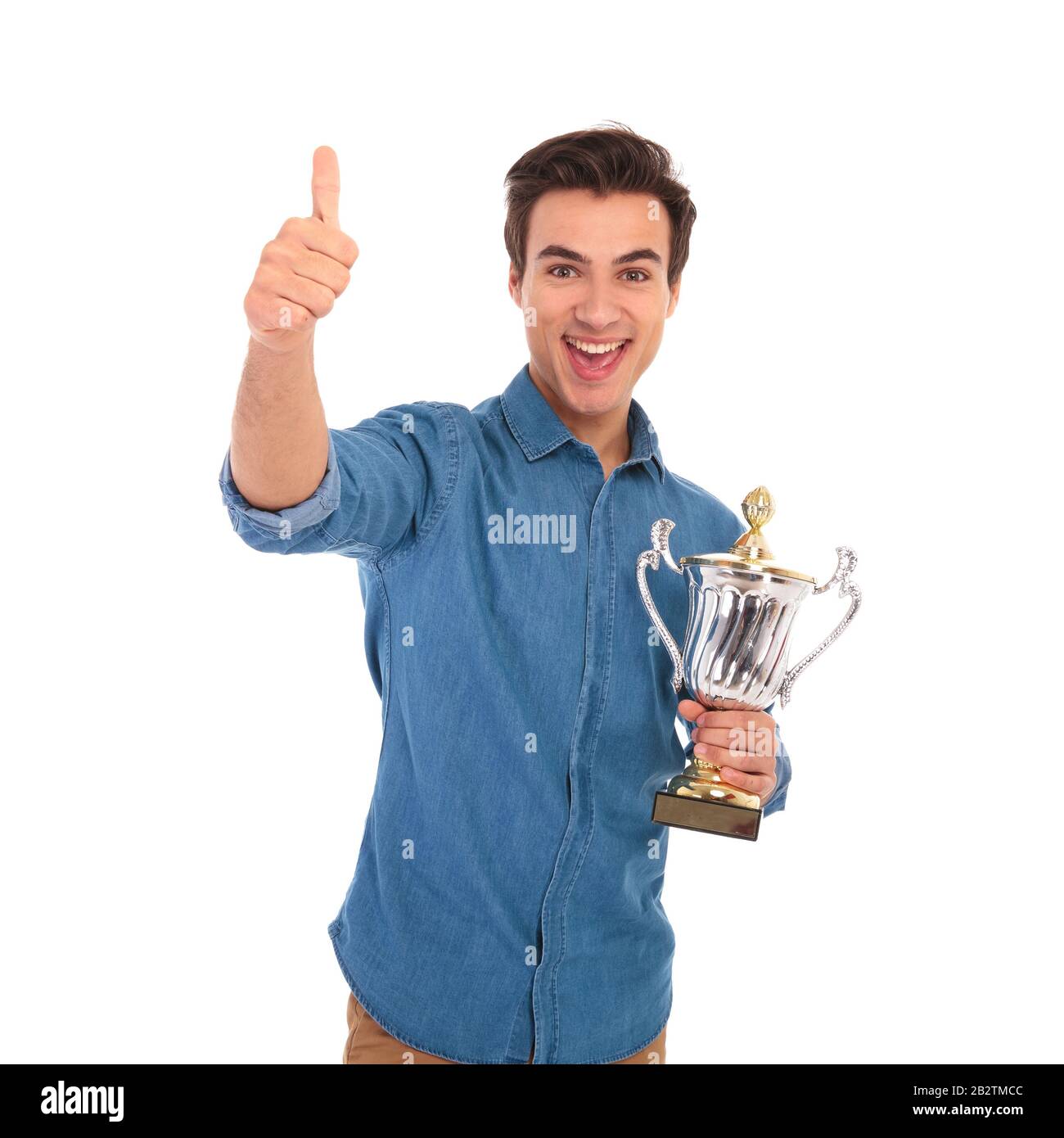 amazed young casual man holding trophy cup and makes the ok thumbs up ...